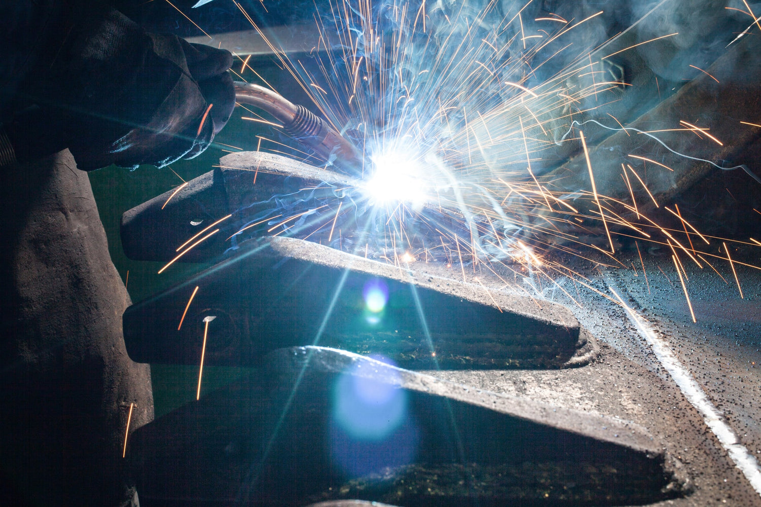 A person welding an excavator bucket working outdoors with sparks flying everywhere
