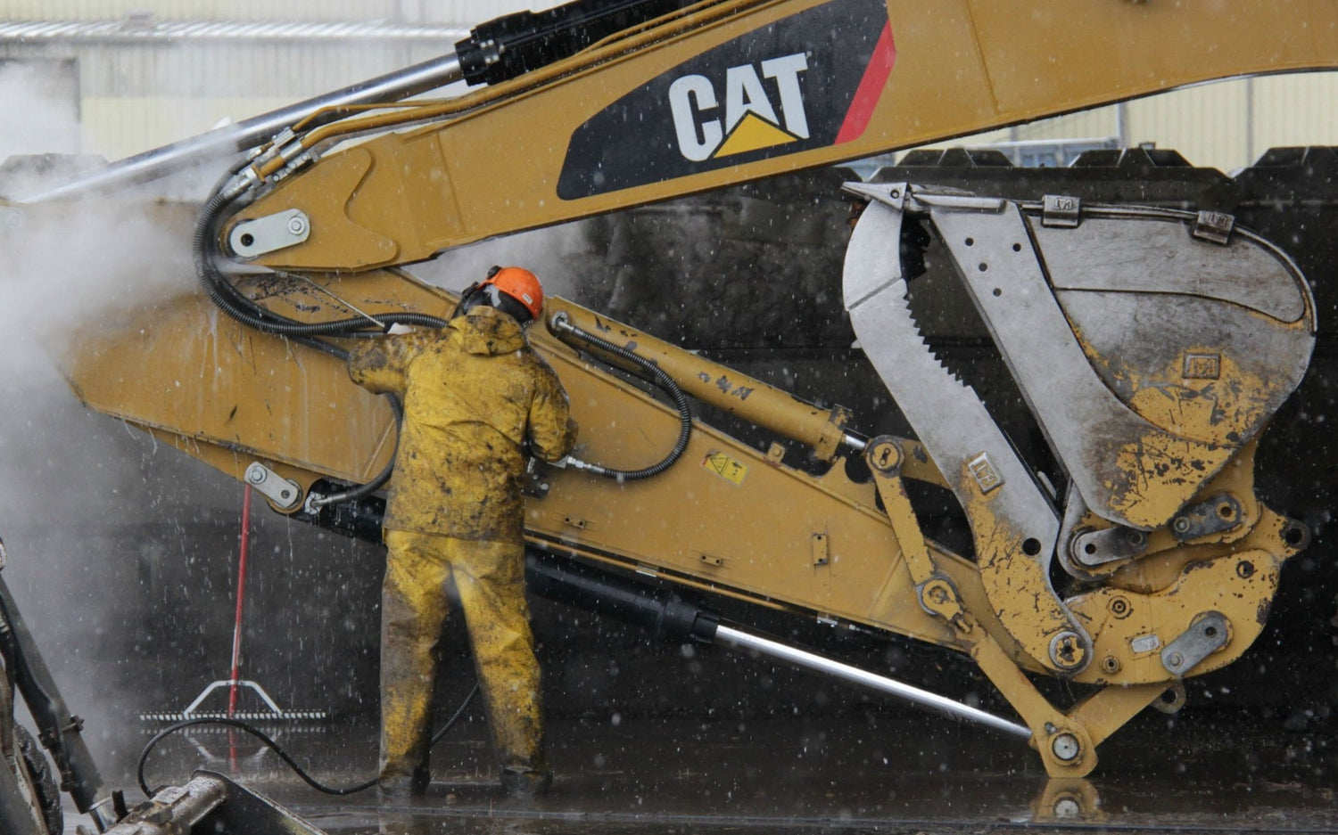 A person in yellow overalls pressure washing an excavator